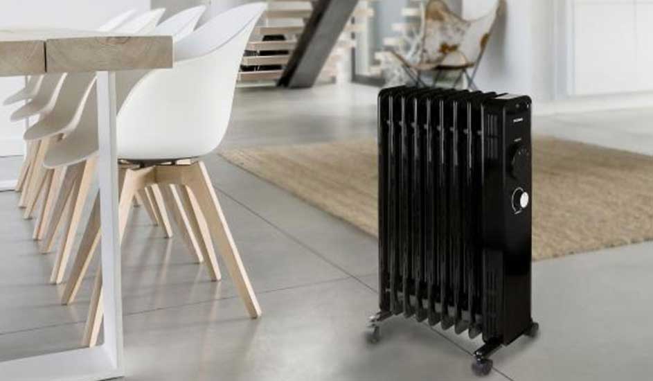 Un radiateur noir à roulettes se tient sur un sol gris clair, près d'une table et de chaises blanches dans une pièce lumineuse.
