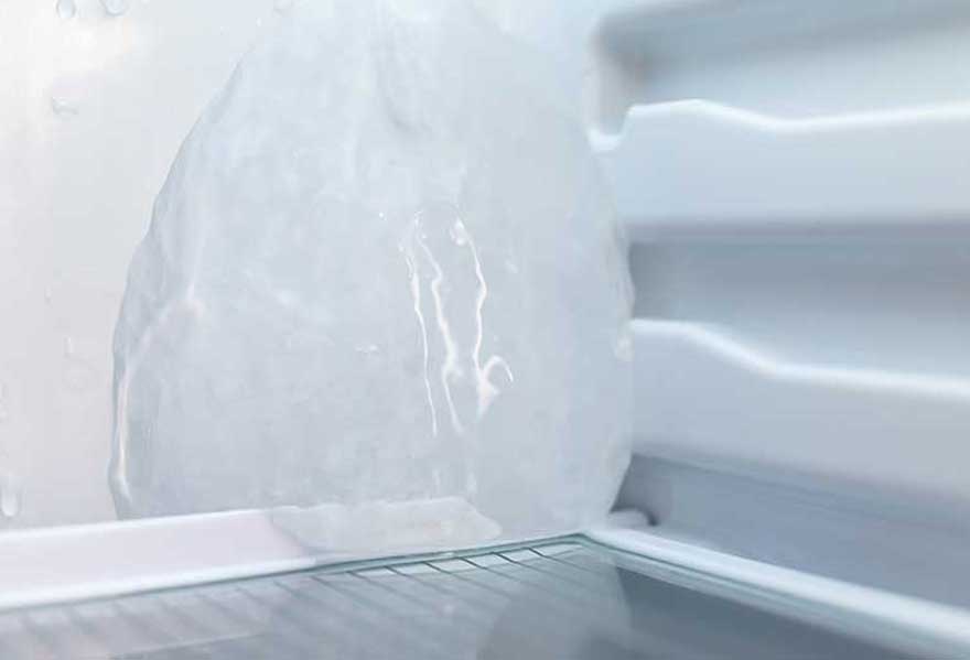Vue d'un réfrigérateur blanc avec une grande masse de glace et une étagère en fil métallique.