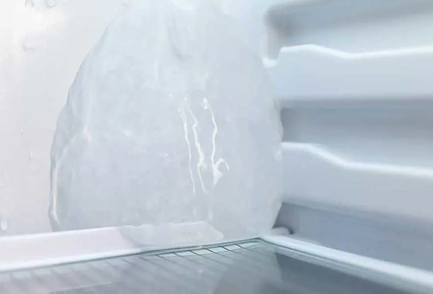 Vue d'un réfrigérateur blanc avec une grande masse de glace et une étagère en fil métallique.
