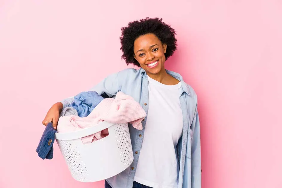 Een witte wasmand vol kleding staat tegen een roze achtergrond.