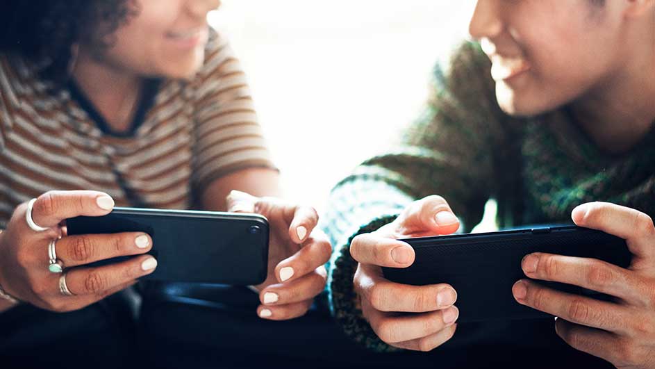 Deux personnes tiennent des smartphones noirs. La personne à gauche porte un T-shirt rayé. La personne à droite porte un pull en maille.