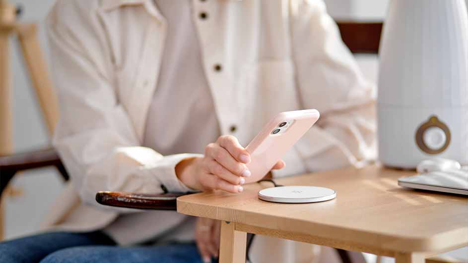 Une table en bois clair avec un téléphone rose, un chargeur sans fil, un humidificateur blanc et un clavier.