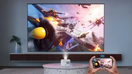 Een projector toont een actiescène, terwijl iemand hem draadloos bedient met een smartphone in een moderne woonkamer.