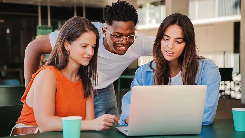 Drie mensen kijken naar een laptop op een groene tafel. Twee blauwe bekers staan aan de zijkant.
