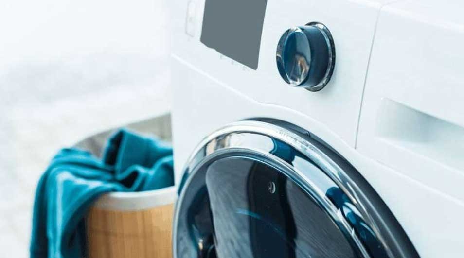 Machine à laver blanche avec linge bleu dans un panier en bois. Panneau de commande visible.