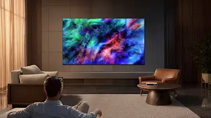 Een man kijkt in een stijlvolle woonkamer naar een grote tv met kleurrijke abstracte beelden en warme sfeerverlichting.
