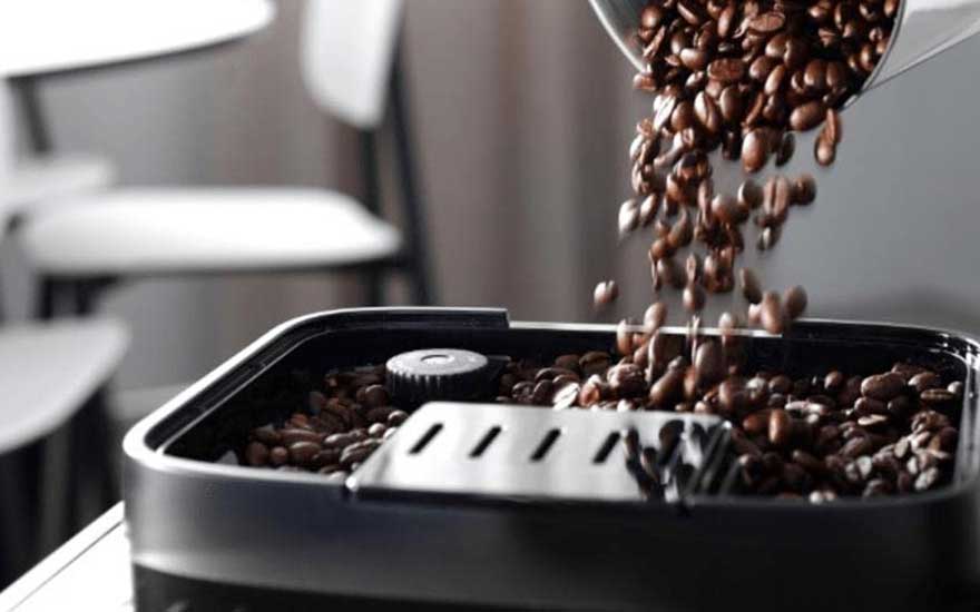 Close-up van aromatische koffiebonen die in de bonenhouder van een koffiemolen worden gegoten, met warme, rijke texturen.