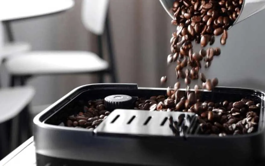 Close-up van aromatische koffiebonen die in de bonenhouder van een koffiemolen worden gegoten, met warme, rijke texturen.