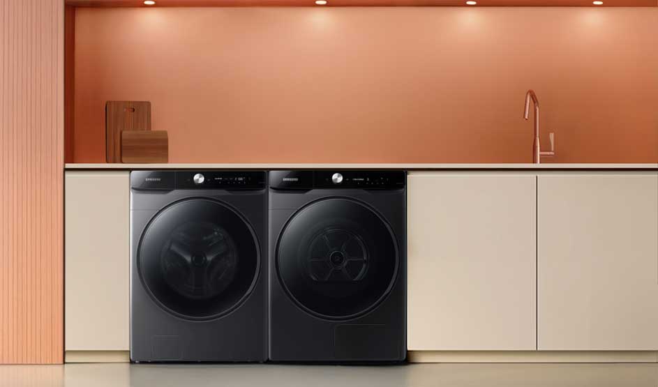 Buanderie minimaliste: deux machines noires à hublot sous un plan blanc, mur rose avec spots, planches en bois et robinet fin à droite.