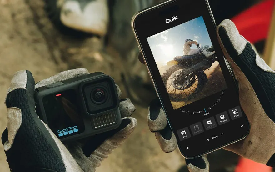 Een zwarte GoPro-camera en een smartphone met de Quik-app worden in handschoenen vastgehouden. Het app-scherm toont een motorfoto.