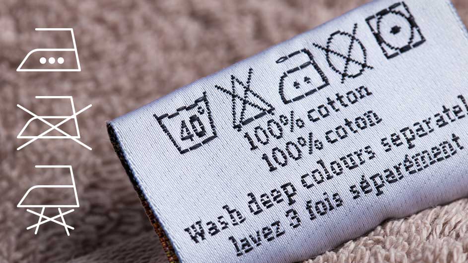 Gros plan d'une étiquette en tissu blanc avec des symboles et du texte d'entretien en noir sur un fond beige.