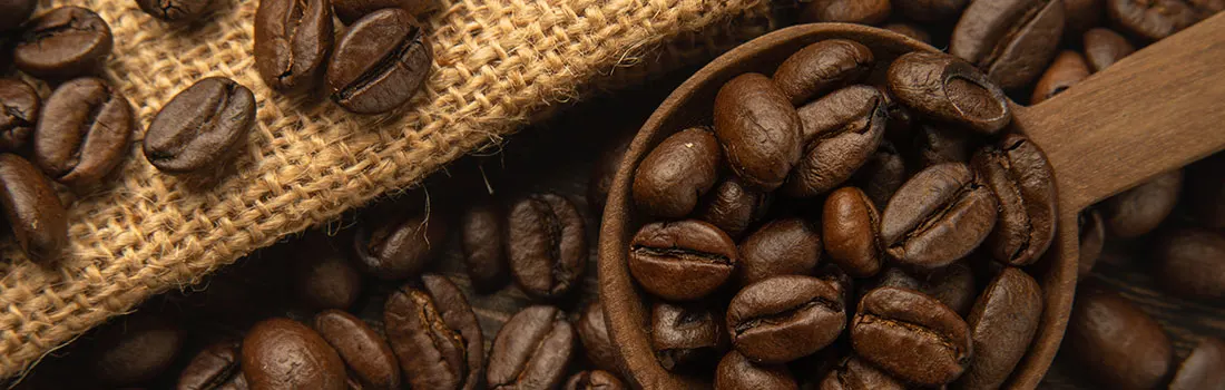 Gros plan sur des grains de café bruns dans une cuillère en bois et sur un sac en toile de jute texturé.