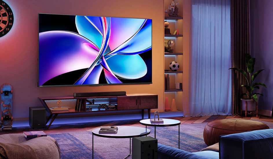 Salon chaleureux avec grande TV aux couleurs néon, meuble bas, tables rondes et éclairage doux autour des étagères.