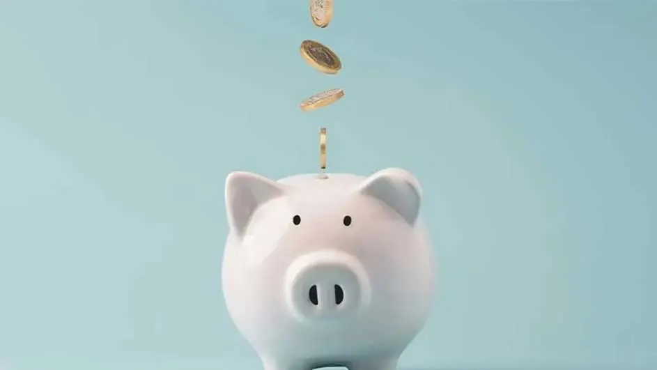 Een witte spaarpot in varkensvorm staat tegen een lichtblauwe achtergrond, met gouden munten die erin vallen.