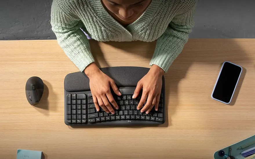 Vue du dessus d'un bureau en bois avec un clavier noir, une souris, et un smartphone.