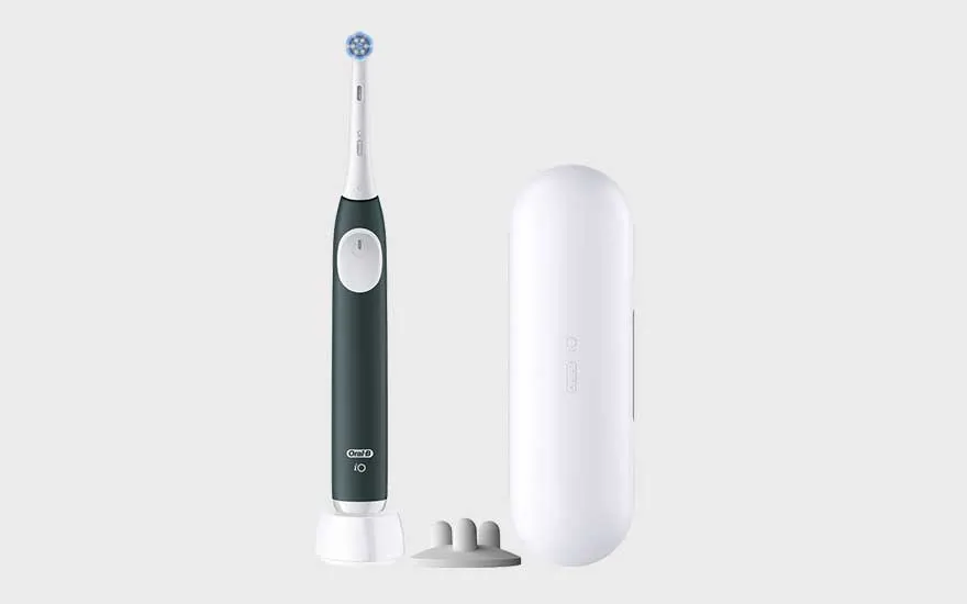 A black electric toothbrush stands upright next to a white charging case and two small attachments.