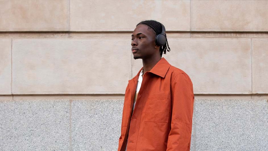 Un homme porte un casque noir et une veste orange devant un mur de pierre beige et gris.