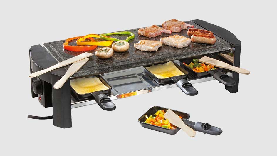 Gril à raclette avec viande, légumes et fromage fondu. Spatules en bois à côté.