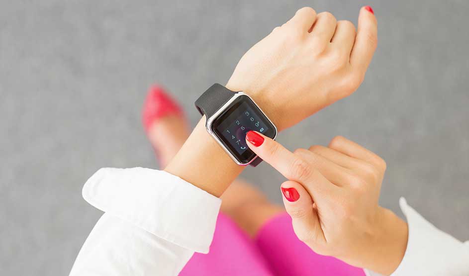 Iemand bedient een smartwatch met touchscreen, met rode nagels en kleurrijke kleding zichtbaar van bovenaf.