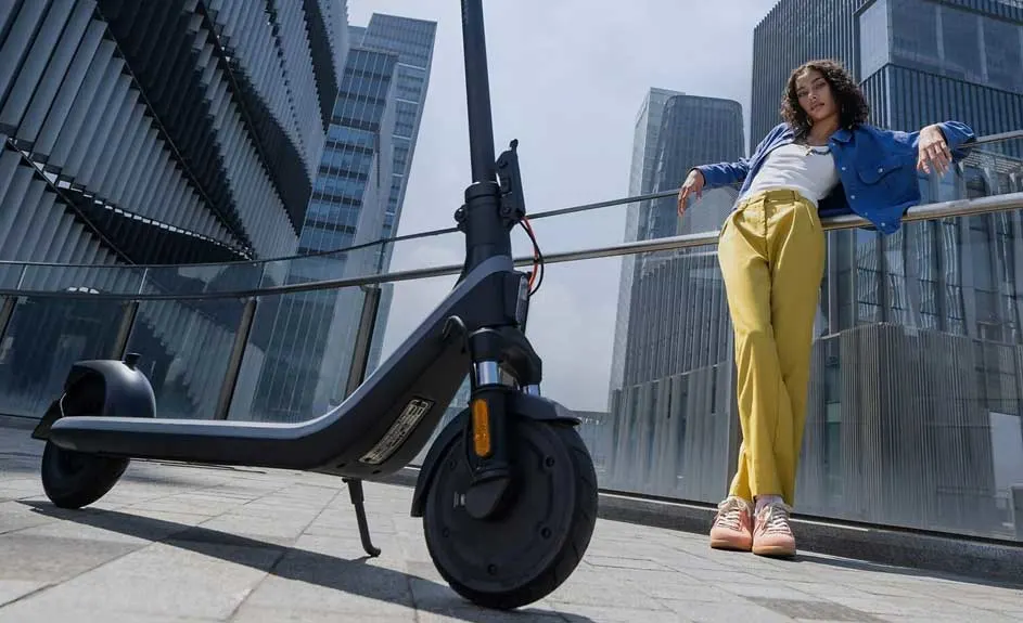 Une trottinette noire est garée sur un trottoir pavé, avec de grands bâtiments en arrière-plan.