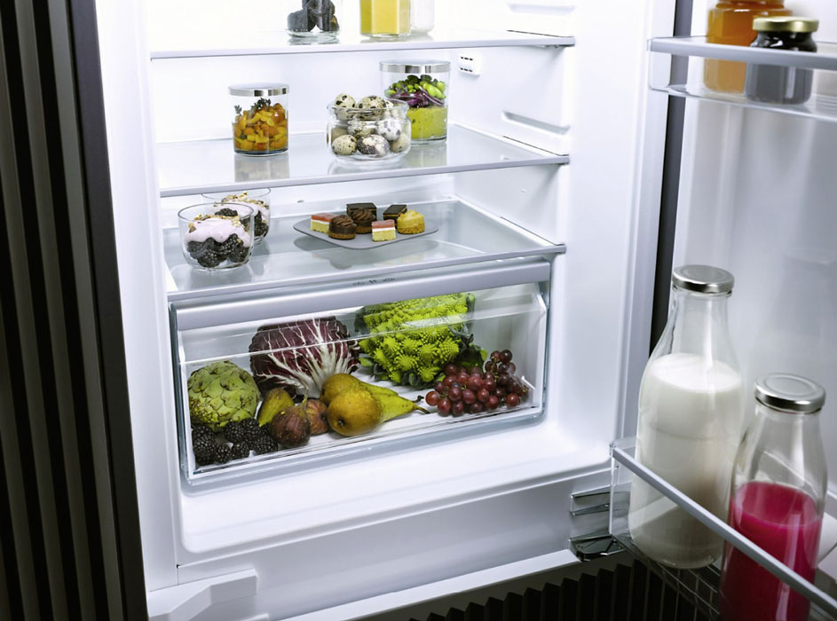 Frigo blanc ouvert montrant des fruits, des légumes, du lait et des desserts sur des étagères.