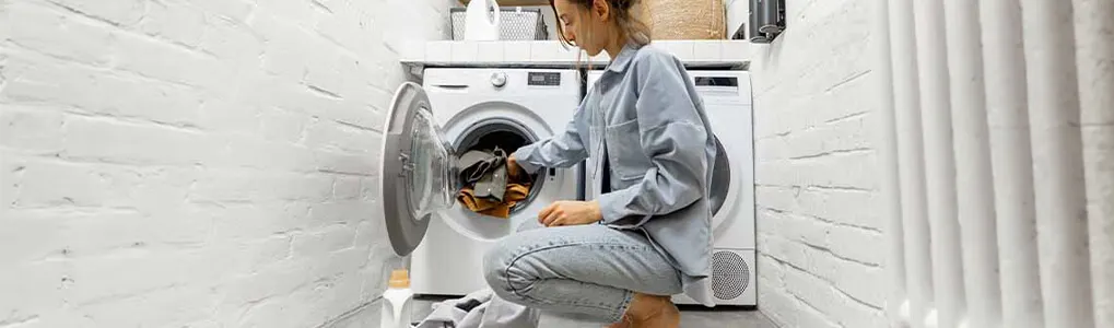 Une buanderie avec une machine à laver blanche ouverte, remplie de linge, sur un sol carrelé.