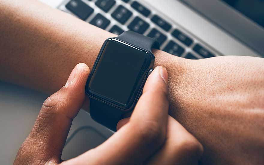 Montre noire au poignet, main touchant l'écran. Clavier d'ordinateur portable visible en arrière-plan.