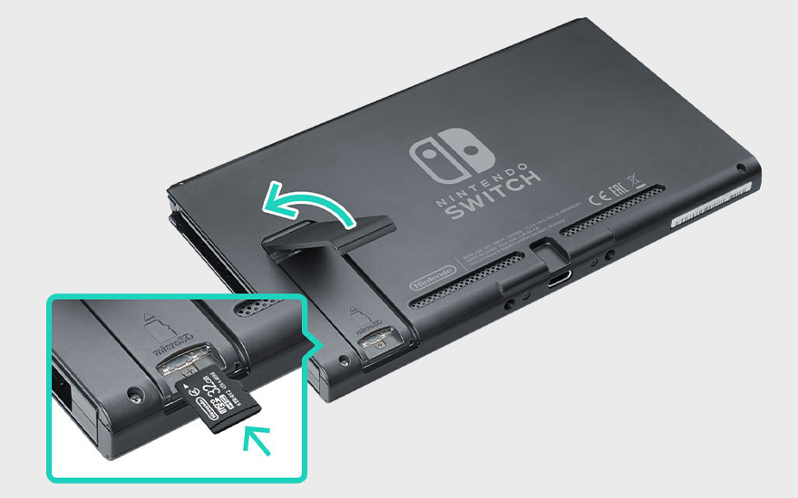 Une Nintendo Switch grise avec une béquille ouverte et une carte MicroSD de 32 Go insérée. Flèches vertes directionnelles.
