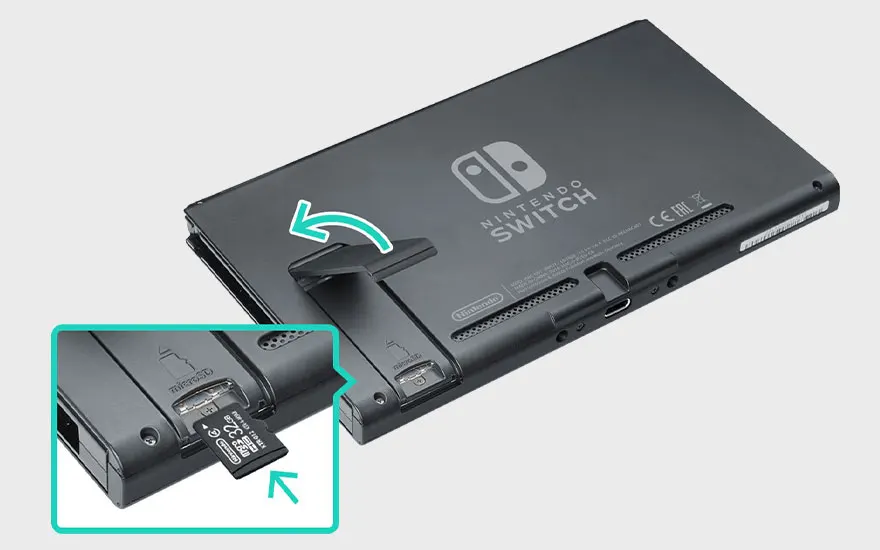 Une Nintendo Switch grise avec une béquille ouverte et une carte MicroSD de 32 Go insérée. Flèches vertes directionnelles.
