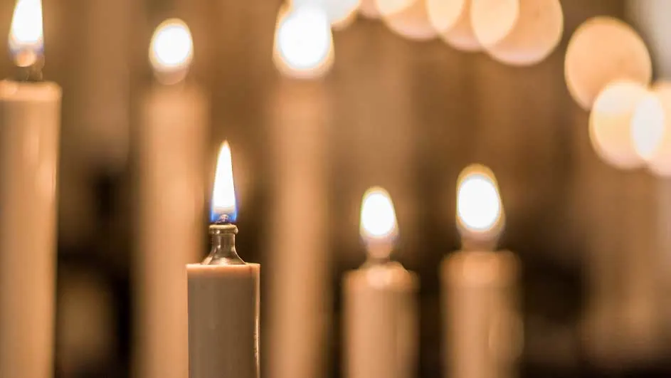Een reeks brandende, crèmekleurige kaarsen met een zachte gloed tegen een warme, bruine achtergrond.