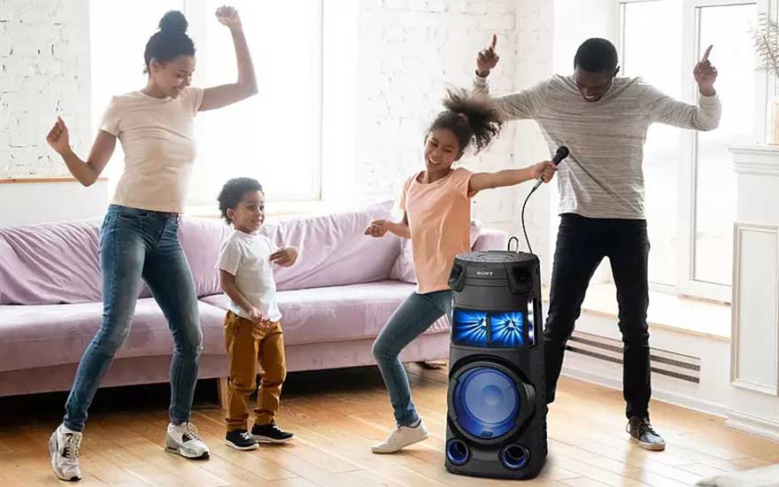 A family dancing next to a black Sony speaker with blue lights in a room. There is a light-purple couch in the background.
