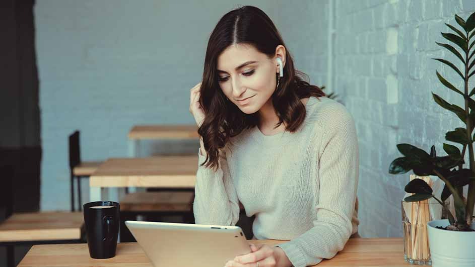 Une tasse noire, une tablette et une plante sont sur une table en bois. Des tables sont à l'arrière-plan, devant un mur bleu.