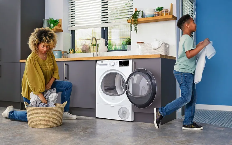 Une buanderie avec un sèche-linge blanc à côté d'une panière à linge en osier sur un sol gris. Une fenêtre est visible au-dessus.