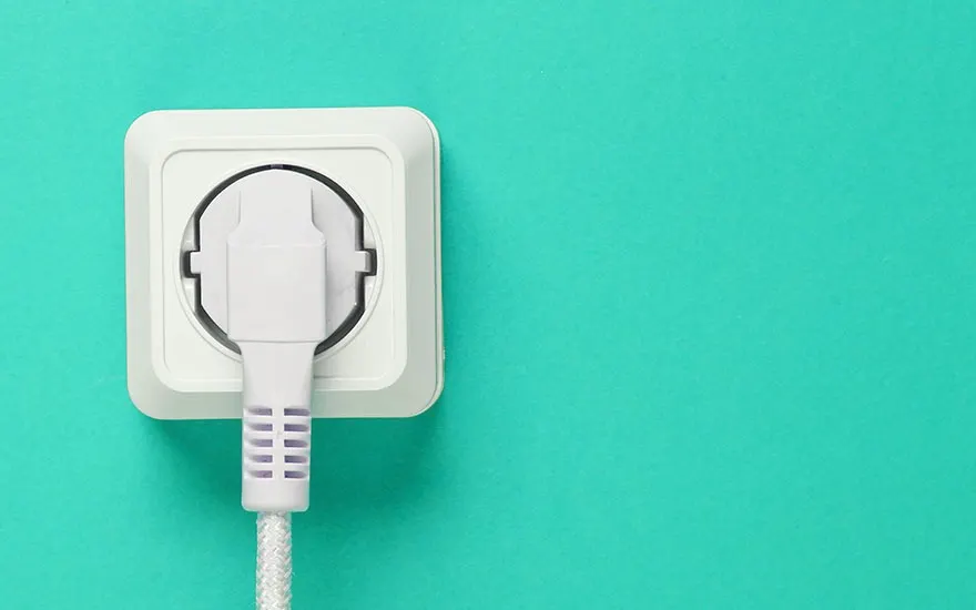 Une prise blanche est branchée sur un mur turquoise, avec un câble tressé blanc visible.