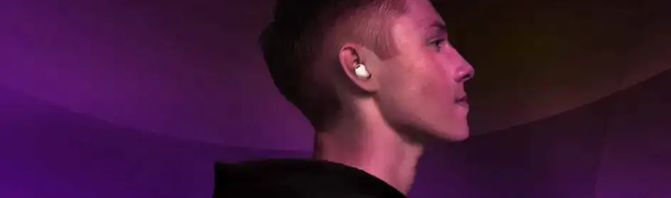 Un écouteur blanc dans l'oreille devant un fond violet dégradé et un vêtement noir.