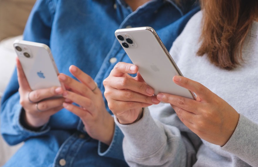 Twee witte smartphones worden vastgehouden door handen tegen een achtergrond van blauwe en grijze kleding.