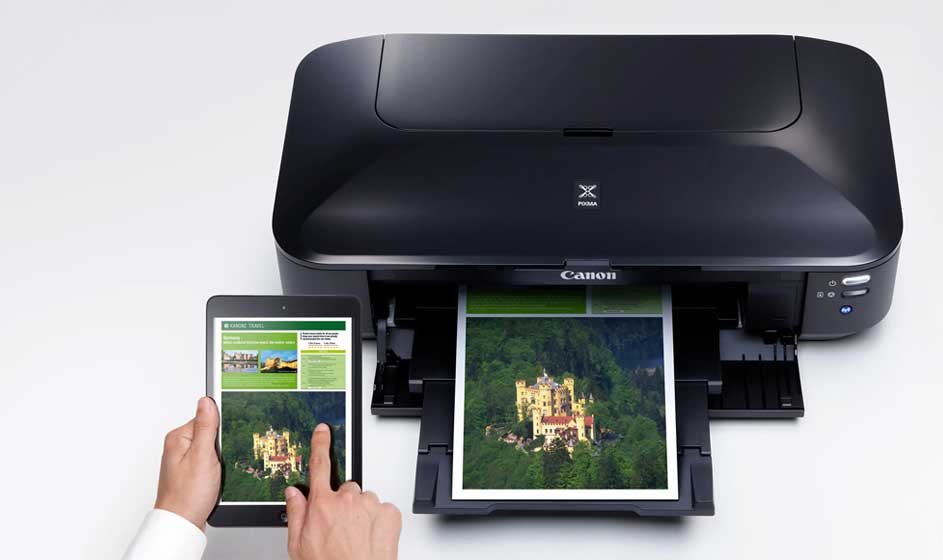 Une imprimante Canon noire imprime une photo colorée. À côté, une personne tient une tablette affichant la même image, sur une surface claire.