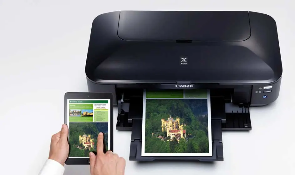 Une imprimante Canon noire imprime une photo colorée. À côté, une personne tient une tablette affichant la même image, sur une surface claire.