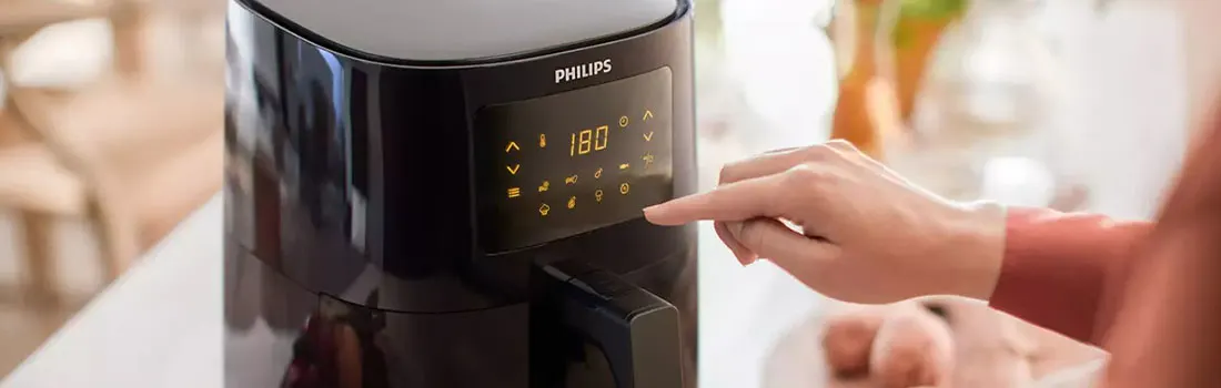 Une friteuse Philips noire affiche 180 °C. Une main appuie sur l'écran tactile.
