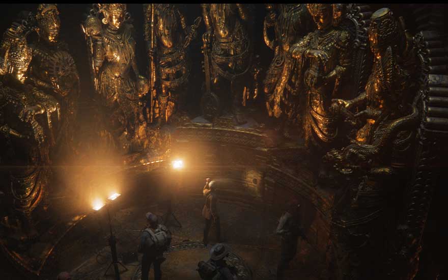 Dans une salle souterraine dorée, des explorateurs observent d’immenses statues sacrées éclairées par de puissants projecteurs.