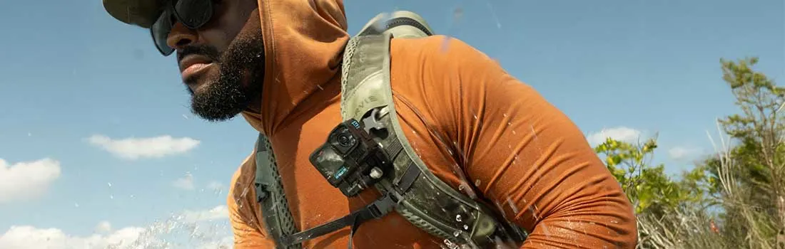 Action camera mounted on a backpack, with a blue sky and trees in the background.