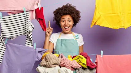 Femme souriante en tablier devant du linge suspendu sur une corde à linge avec des pinces à linge sur fond mauve.