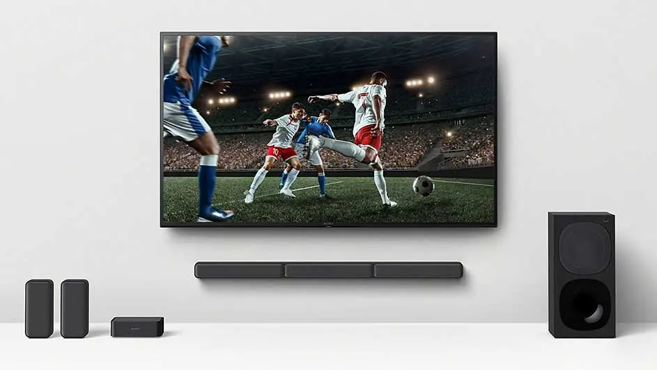 Téléviseur affichant un match de football, avec barre de son et haut-parleurs noirs sur un mur blanc.