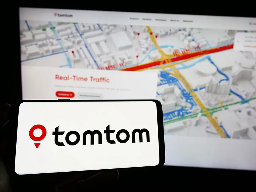 Écran de smartphone affichant le logo TomTom en rouge et noir, avec une carte de navigation détaillée en arrière-plan.