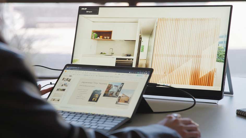 Un ordinateur portable et un écran affichent des images de design d'intérieur sur un bureau blanc, près d'une fenêtre.