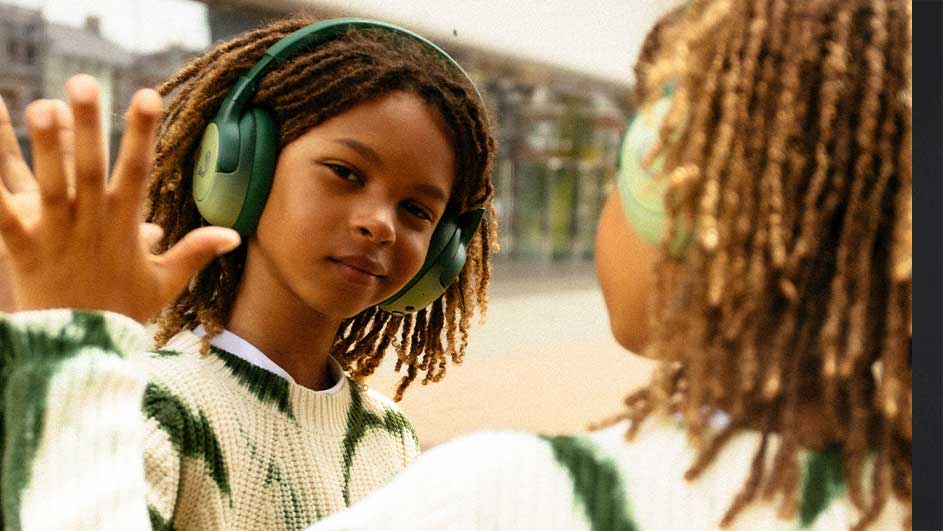 Twee mensen met dreadlocks en groene hoofdtelefoons staan tegenover elkaar, op de achtergrond een gebouw.