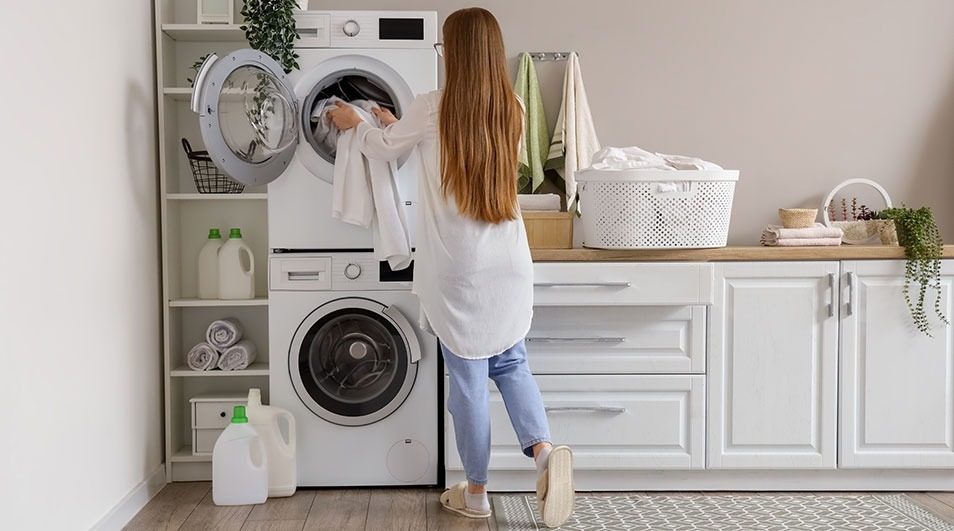 A laundry room shows a stacked washer and dryer, white cabinets, and shelves with supplies.