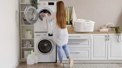 A laundry room shows a stacked washer and dryer, white cabinets, and shelves with supplies.