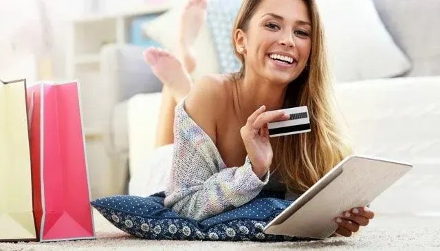 Een tablet en een creditcard worden vastgehouden, met boodschappentassen op de achtergrond.