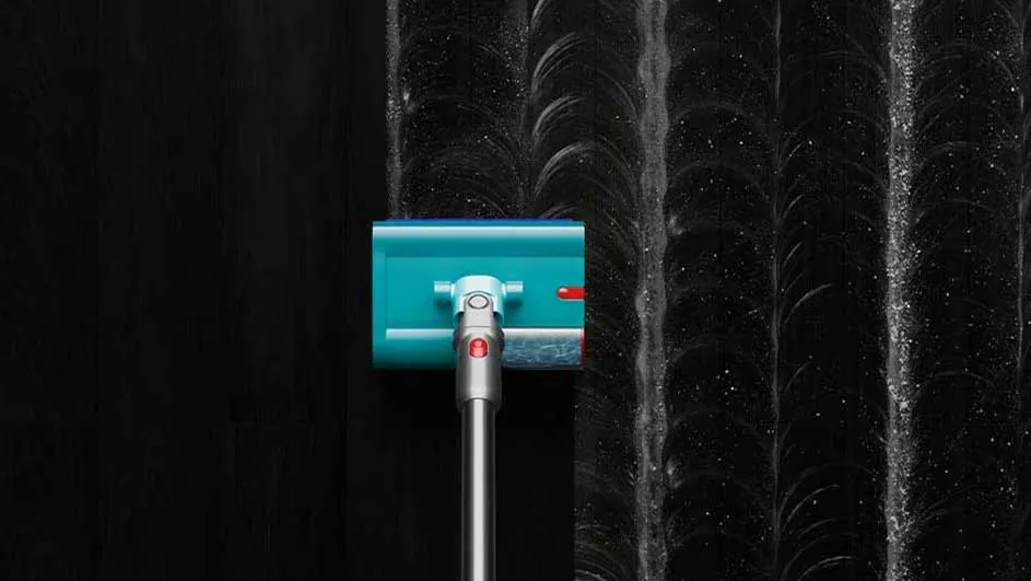 Un aspirateur turquoise nettoie une surface noire, laissant des traces brillantes.